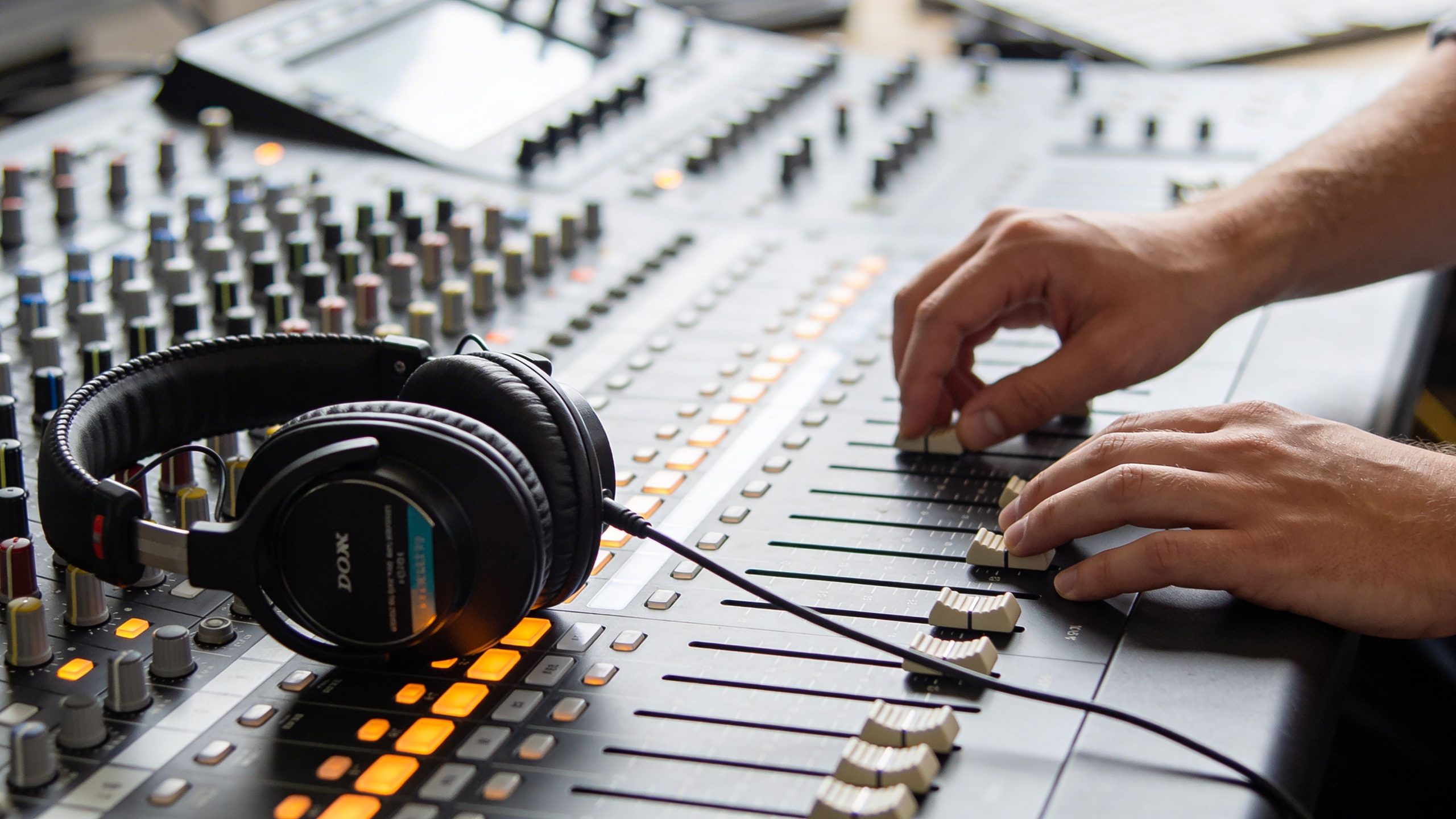 A close-up shot of a person adjusting faders on a professional audio mixing console with headphones nearby.